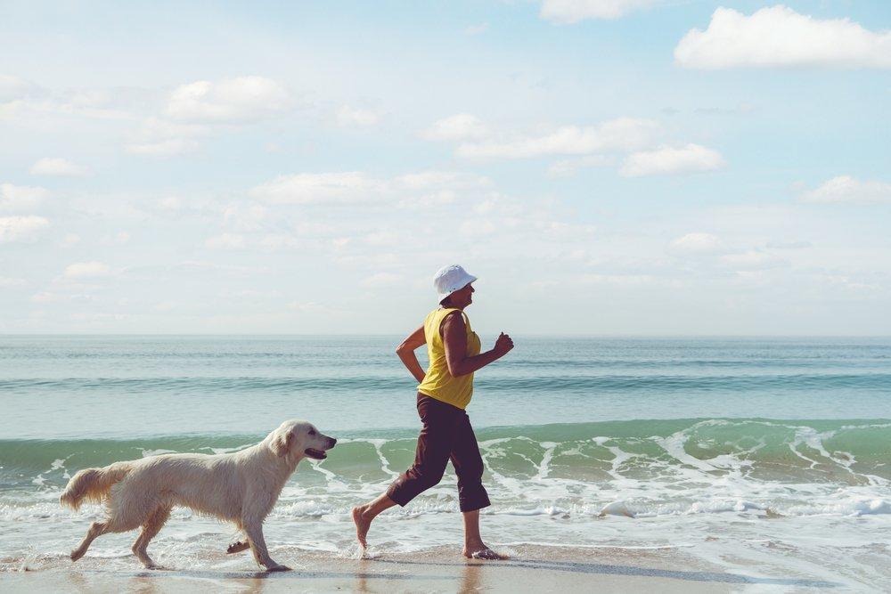 A senior woman goes for a run on the beach with her dog